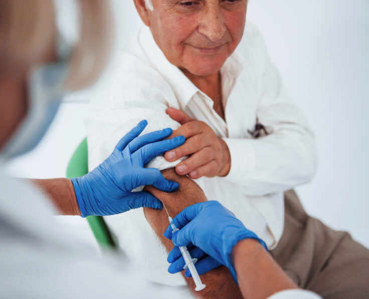 Female doctor injecting senior male patient with syringe in the clinic.